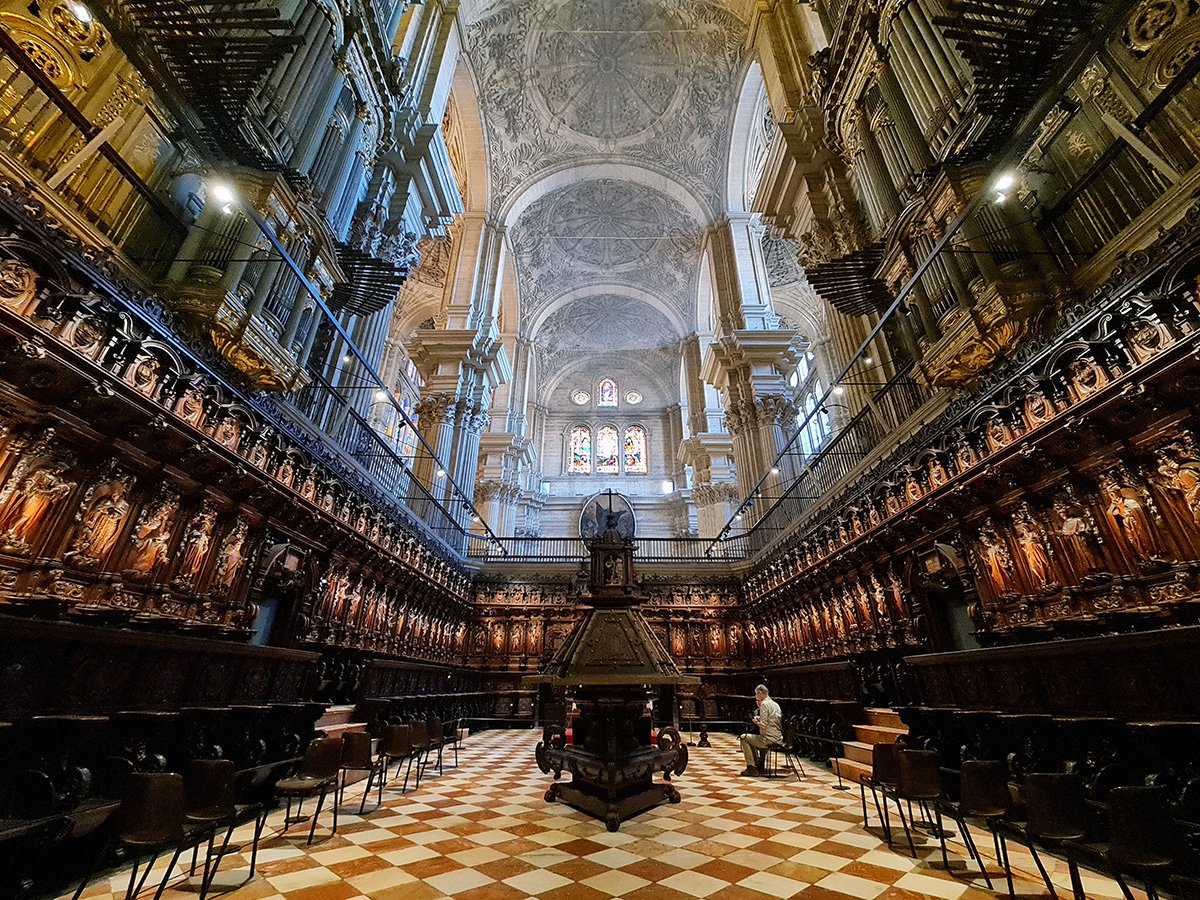 De Kathedraal van Málaga met zijn indrukwekkende gevel en unieke, onvoltooide toren, omgeven door weelderige tuinen, onder een helderblauwe hemel.