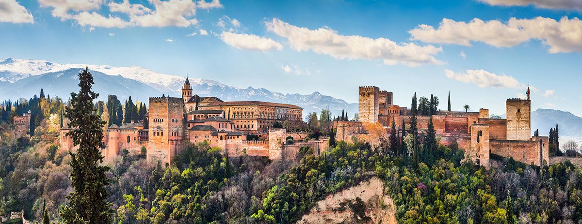 Een panoramisch uitzicht op Granada met de Alhambra en de Sierra Nevada op de achtergrond, onder een betoverende hemel bij zonsondergang.