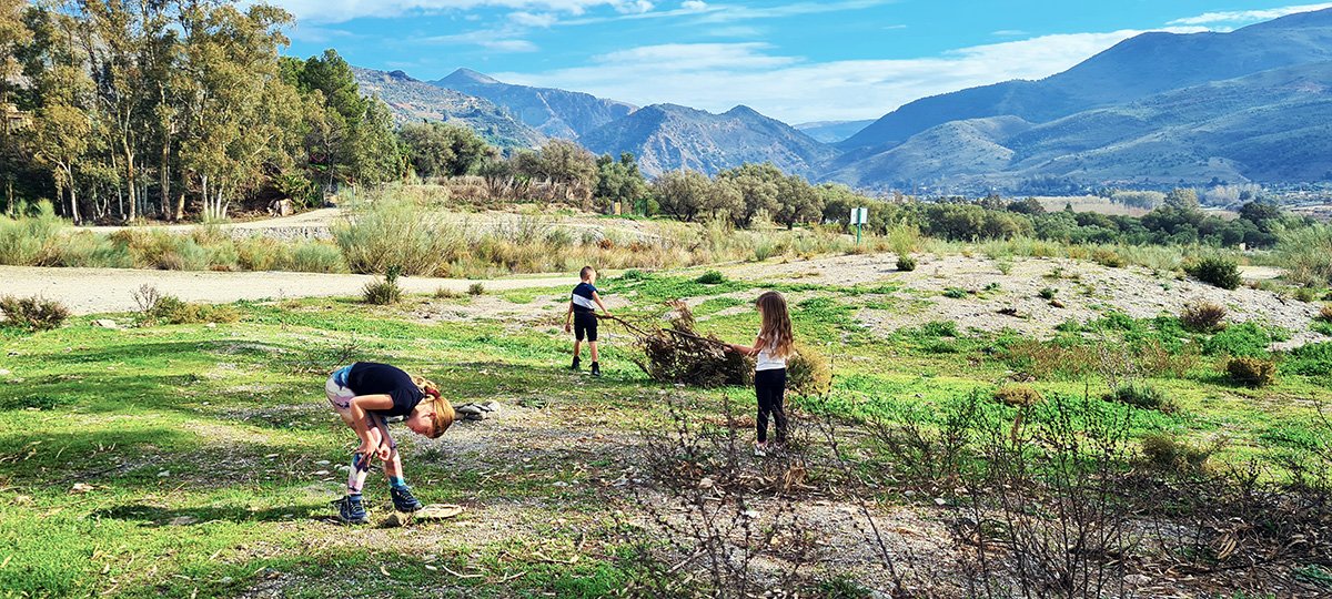 Drie kinderen spelen op een open vlakte bij een camping in Órgiva, omringd door de indrukwekkende bergen van de Sierra Nevada, genietend van de vrijheid en het avontuur.