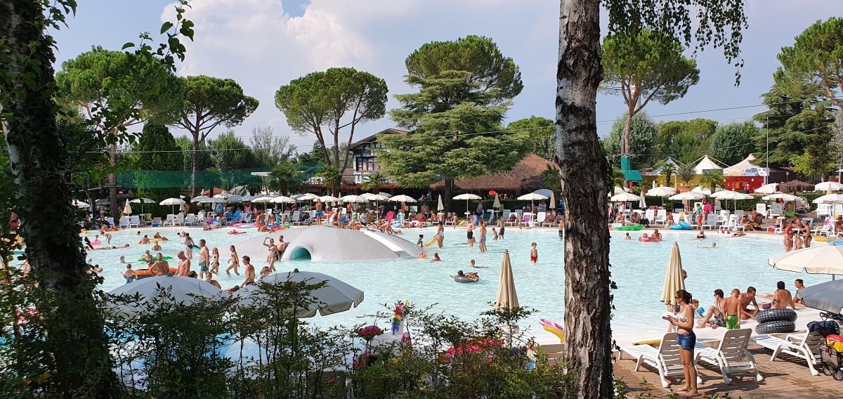 Levendige zwembaddrukte bij Camping HU Altomincio Village aan het Gardameer, omgeven door groen en met gezinnen die genieten van het water.
